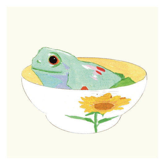 a green frog with pink and red spots sitting in a sunflower decorated teacup on a neutral ivory background